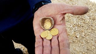 An archaeologist holds 7 gold coins and a sharp of the broken pot they were found in.