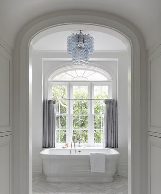 A white bathroom with blue glass chandelier over a freestanding tub