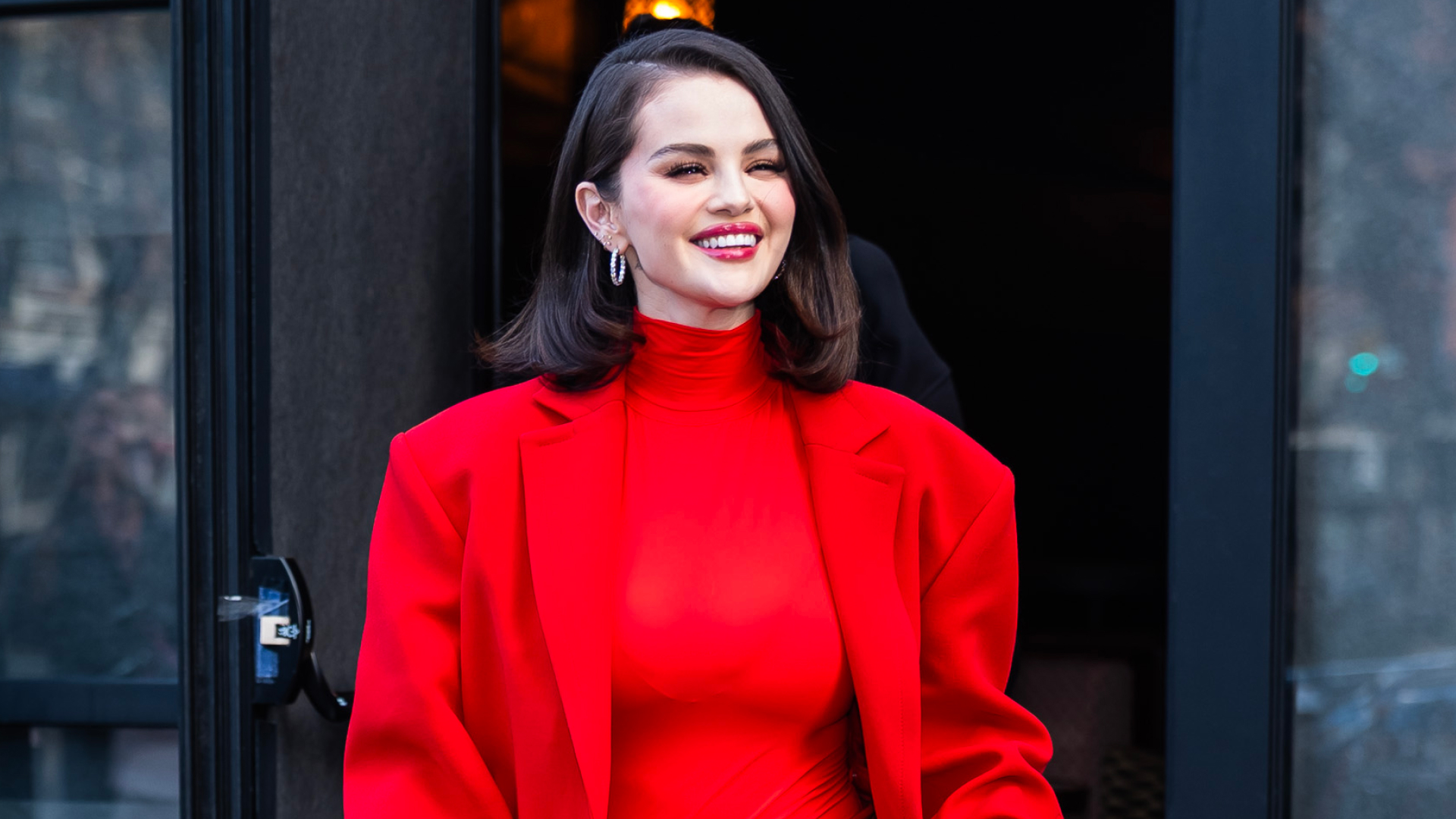 Selena Gomez wearing a lob hairstyle and a red suit smiling for the camera