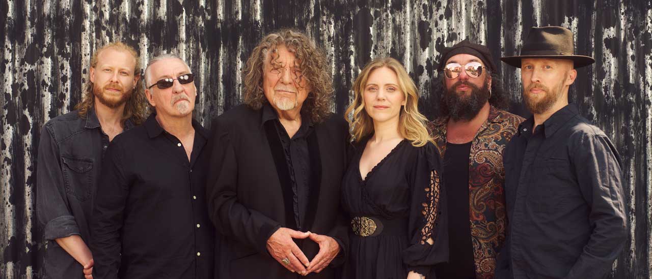 Robert Plant and Saving Grace standing against a corrugated fence