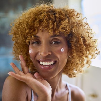 Best moisturiser for mature skin - woman with curly hair applying face cream while smiling