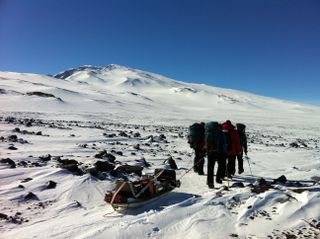 The POLENET/ANET field team drags equipment to install remote seismic and GPS stations at Mount Sidley, a volcano in Antarctica (seen in background).
