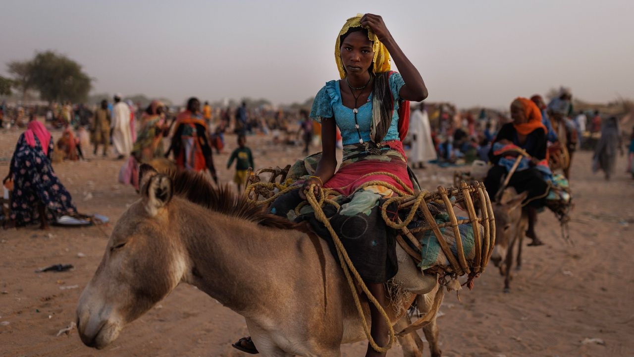 A woman displaced from Sudan&#039;s Darfur region sits on a donkey at a refugee settlement over the border in Adre, Chad