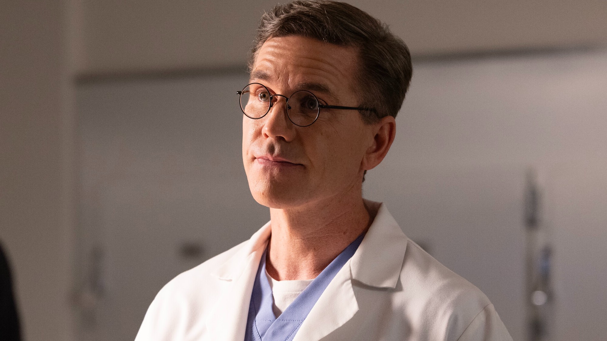 Jimmy talking about birthdays with Tony in the morgue. He's wearing a white lab coat and his signature wire-frame glasses. 