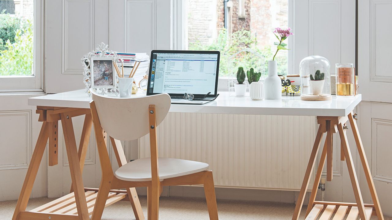 A home office with a Scandi-style desk and chair in white and light wood facing the window and an open laptop on the desk