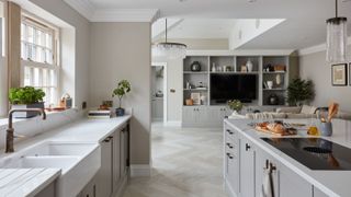 A large open plan kitchen living room spavce with grey cabinetsand built in, a white farmhouse sink, kitchen island, and black t-bar cabinet handles