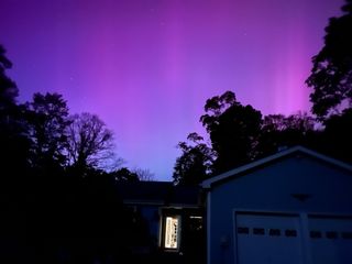 Purple hued auroral lights over a a house and dark trees