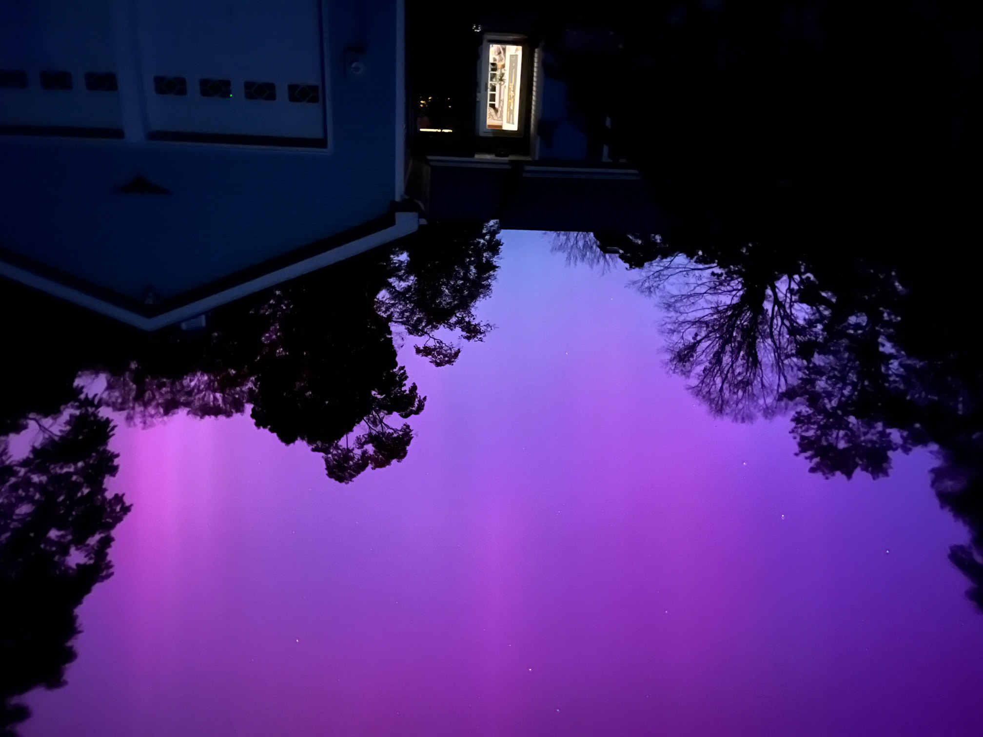 Purple hued auroral lights over a a house and dark trees