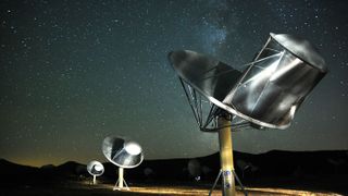 spot-lit satellite dishes on an arid landscape point skyward ere the backdrop of a starry night