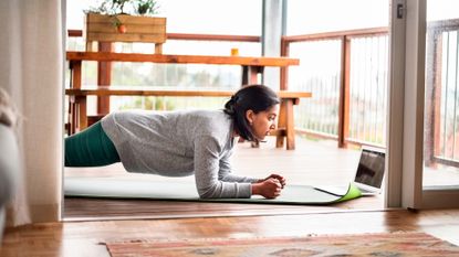 Woman holds plank position on balcony. She is looking at a laptop on the floor in front of her