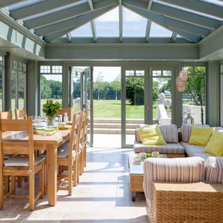 A large green conservatory extension with a striped sofa and wooden dining table