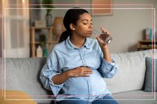 Woman drinking water on the sofa whilst experiencing hot flashes in pregnancy