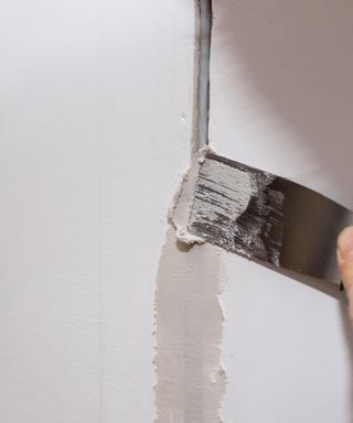 A crack in a white plaster wall being repaired