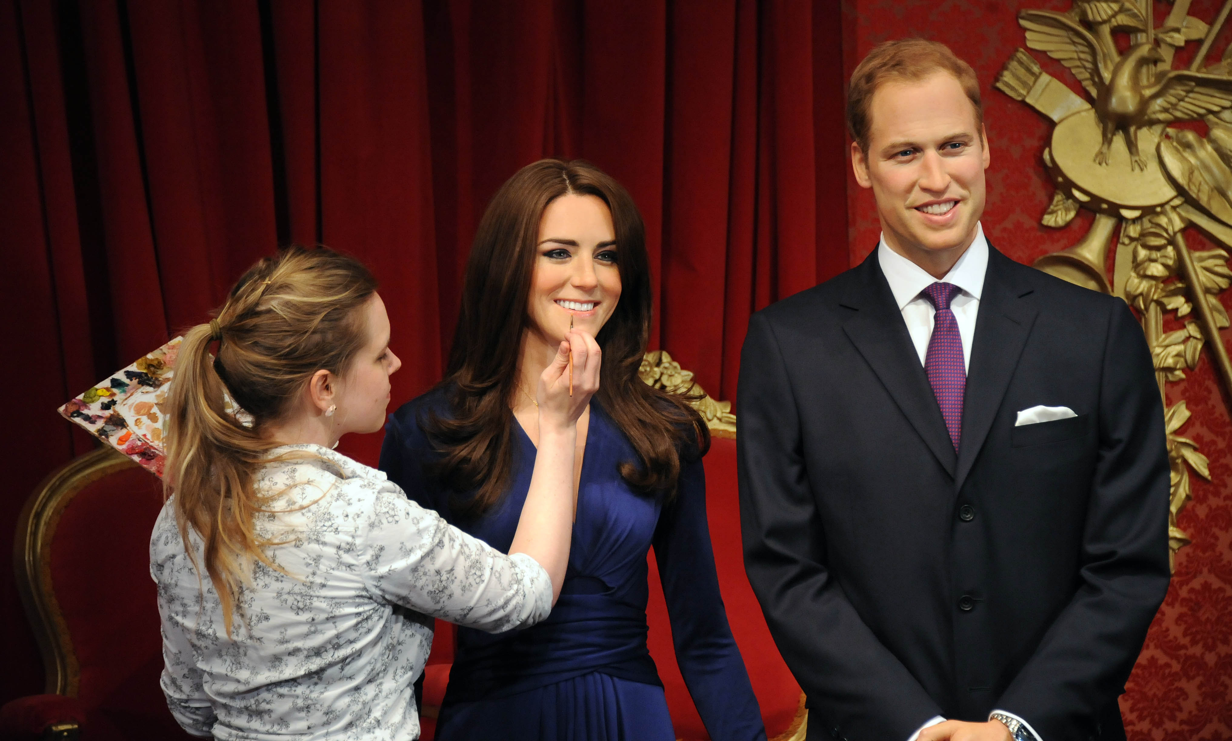 A woman painting a wax figure of Kate Middleton, which is standing next to a wax Prince William