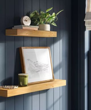 Two wooden floating shelves with decor on, on a dark blue background