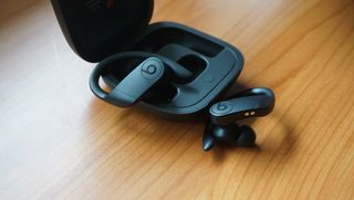 The Beats Powerbeats Pro earbuds pictured with their charging case on a wooden surface