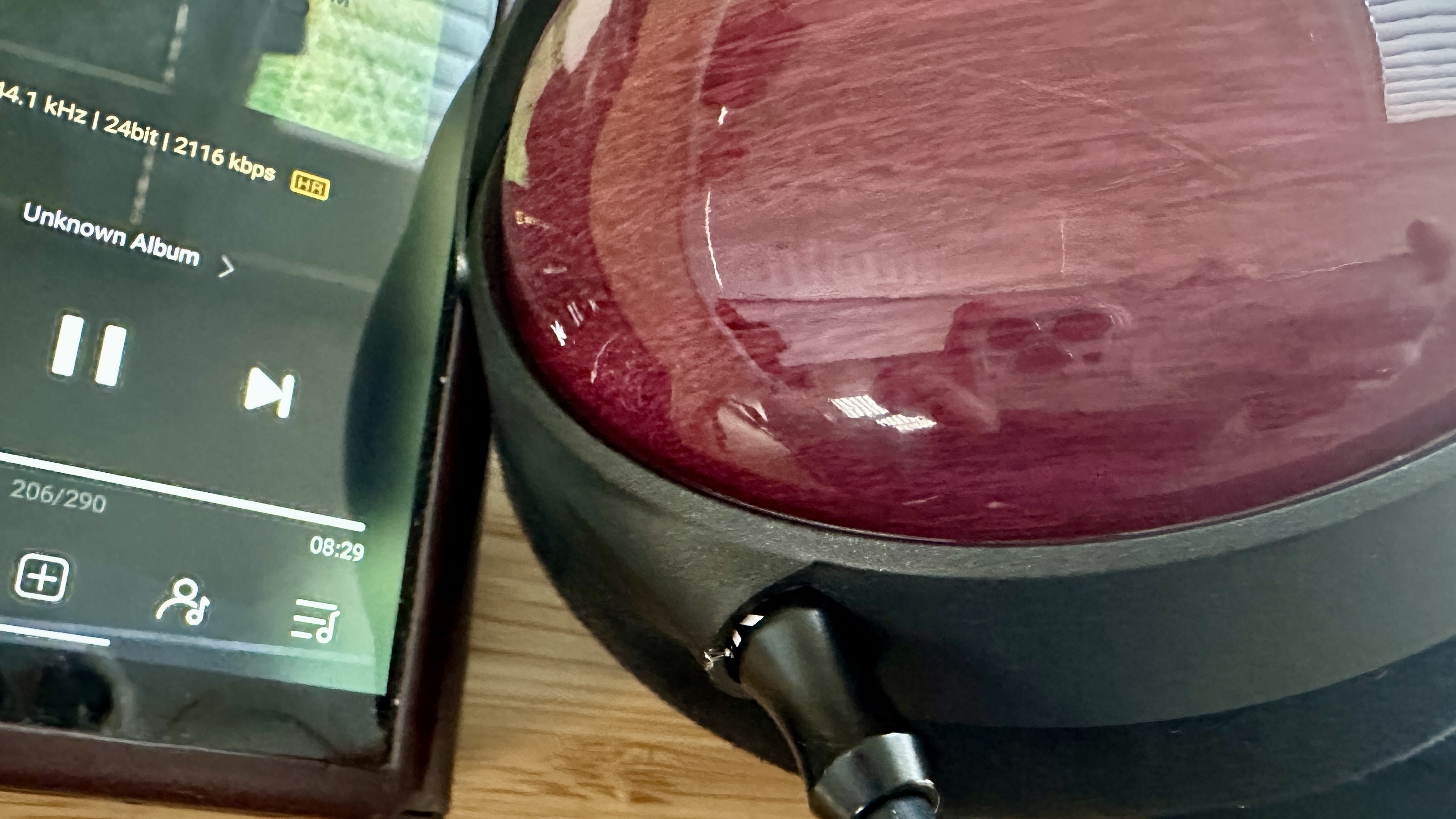 Earcups of the FiiO FT13 closed-back over-ear wired headphones, connected to a portable music player, on a wooden surface.