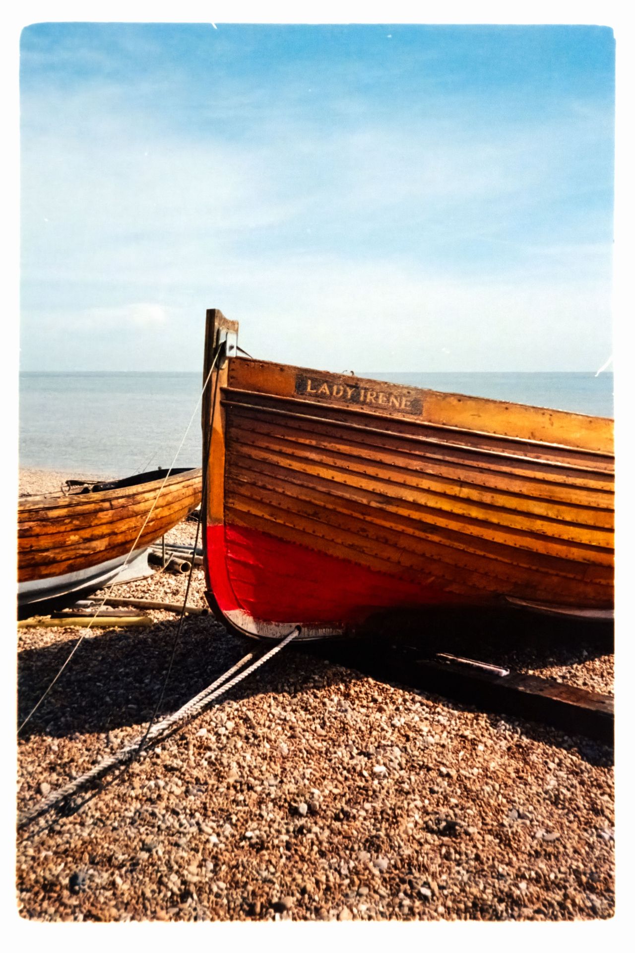 Scanned film photograph of a wooden boat named Lady Irene resting on a pebble beach beside the sea.