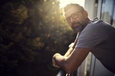 Portrait of casual mature man on balcony. The sun is behind him and his mood is thoughful or sombre.