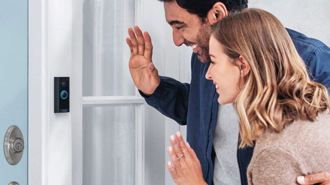 Ring Video Doorbell Wired mounted to door with male and female visitors waving