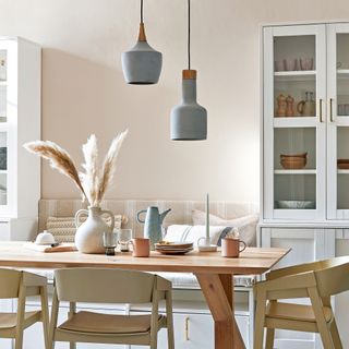 Neutral dining room with tall cupboards either side of bench seating and soft blue pendant lights over the table