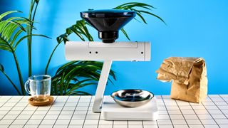 the acaia orion coffee bean doser is a white sci-fi-inspired bean doser with a rotating dial and LED screen and a bean hopper photographed against a blue tom's guide background