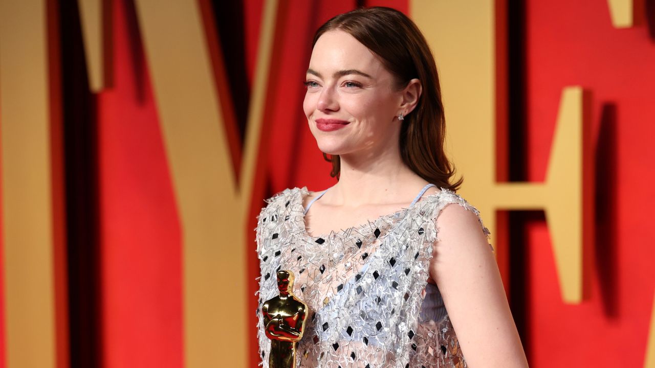 Emma Stone on the Oscars 2024 red carpet holding her award in a sparkly dress