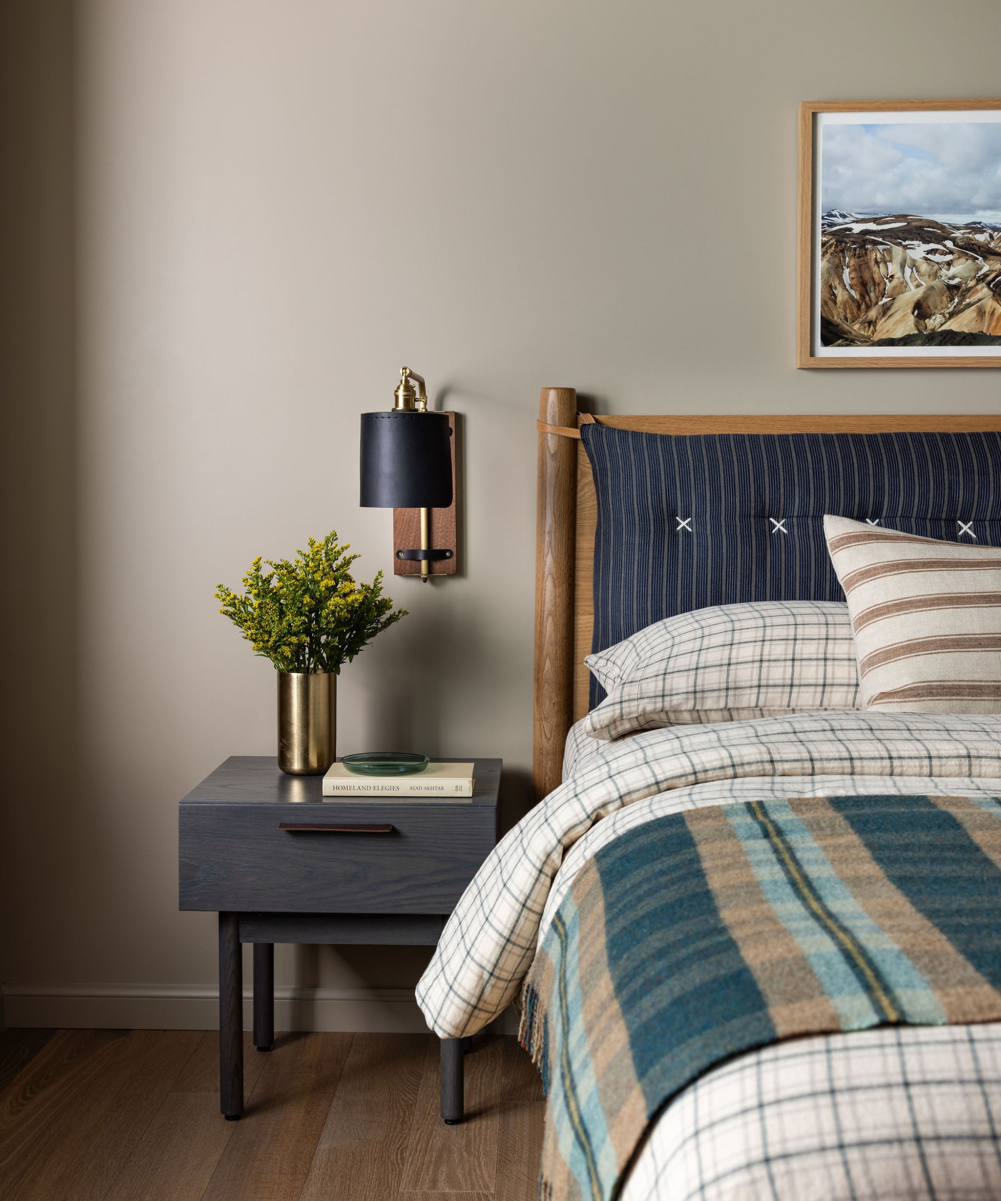 Boy’s bedroom with a blue striped headboard, checked bedding, plaid throw, dark wood nightstand and landscape photograph.