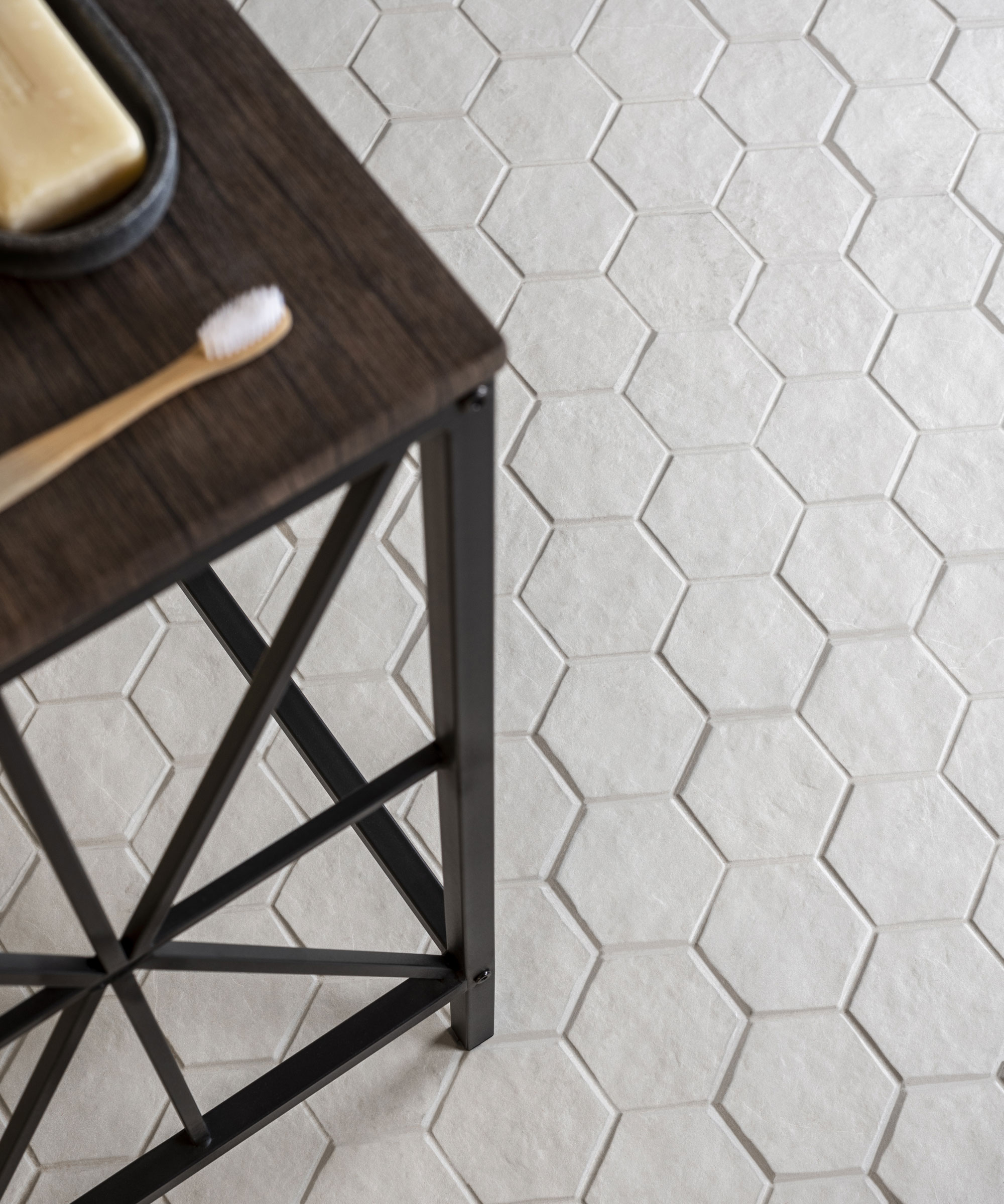 A close-up shot of small, white hexagonal floor tiles under a wooden table with a toothbrush