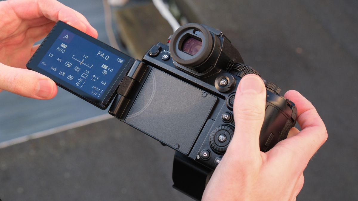 Panasonic Lumix S1R II camera held in a person's hands. The screen is flipped out and a menu displayed on the screen