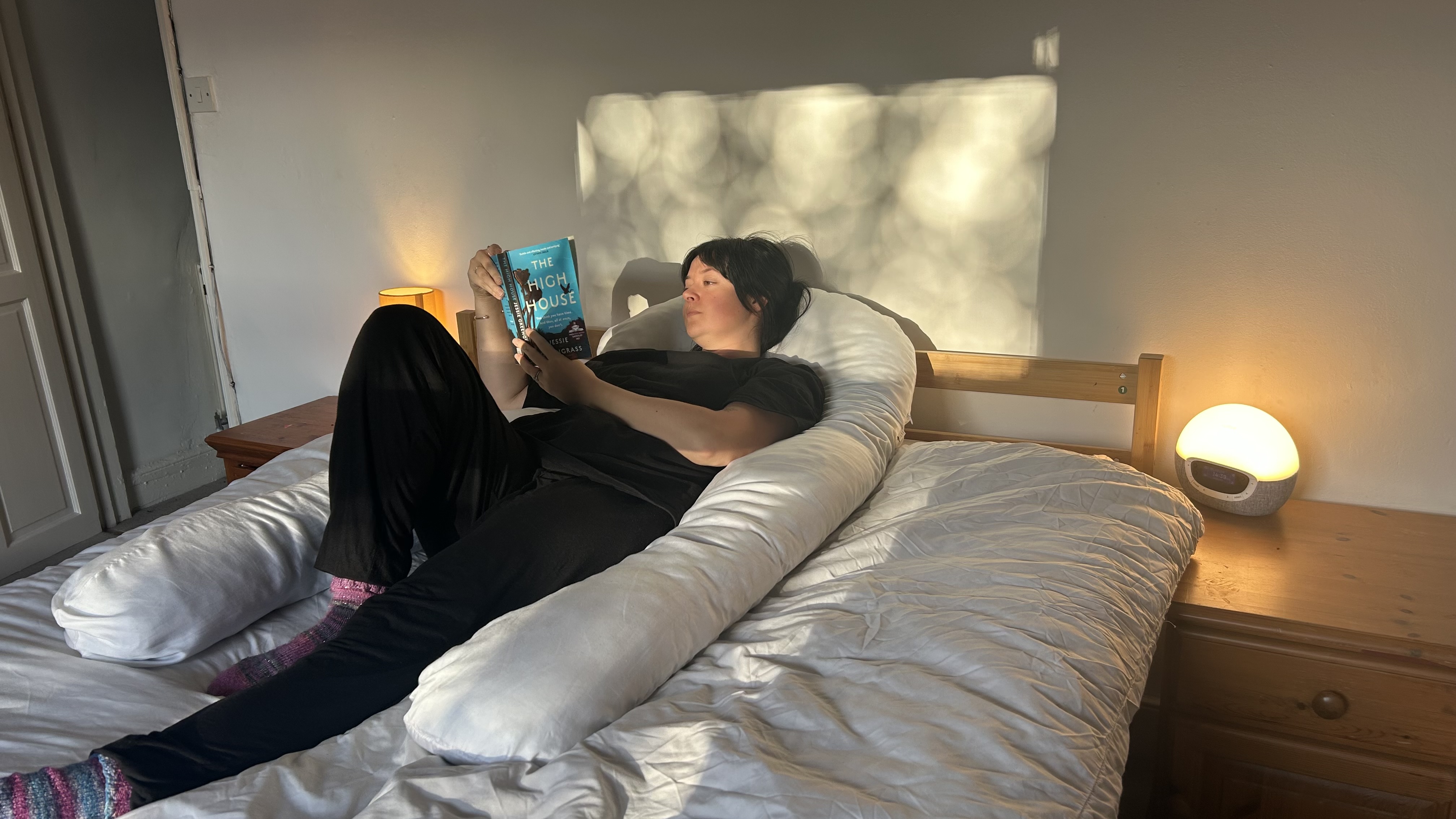 Tom&#039;s guide Sleep Features Editor lying on her back reading a book using the Yana 360&amp;deg; Body Pillow.