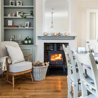 White armchair and table next to stove log burner with storage basket of logs
