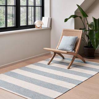 A striped blue and white rug on a wooden floor with a minimalist wooden lounge chair