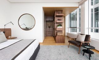 In the second bedroom, custom millwork in American wlnut timber, solid and veneered, is combined with soft additions including throws and cushins by Jim Thompson and an Omar Khan rug. A circular mirror by Holly Hunt is hung on the wall.