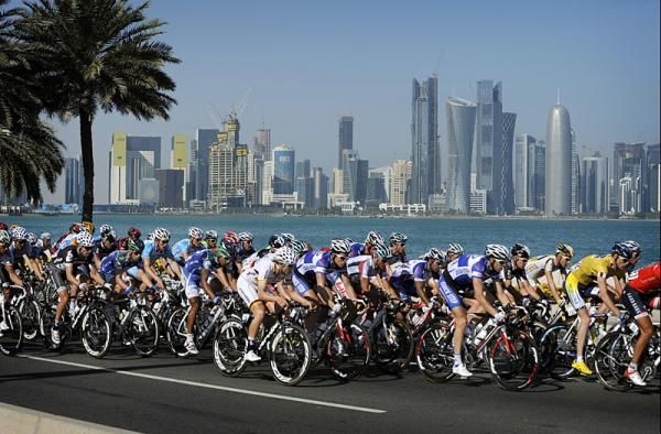 The peloton rides with the skyline of Doha in the background.