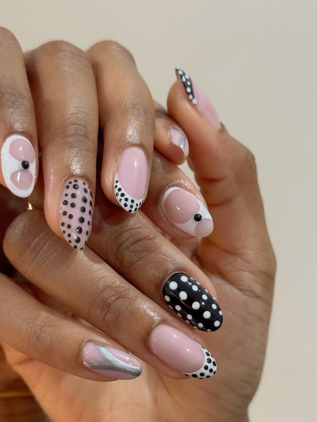 Close-up photo of a person&amp;rsquo;s hands showcasing black and white polka dot nail art on almond nails.