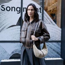 Alexa Chung wears a brown leather bomber jacket with a grey pleated skirt.