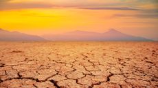 Cracked brown dirt is seen with mountains and yellow haze in the background