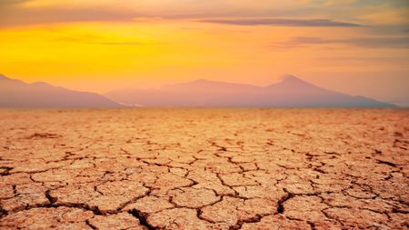 Cracked brown dirt is seen with mountains and yellow haze in the background