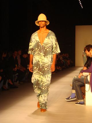 Male model on runway wearing a safari-print jumpsuit and low hat