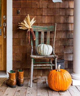 An orange pumpkin and a white pumpkin on a chair on a porch outside