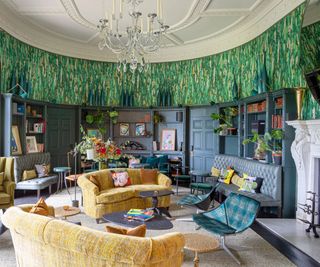 rounded living room with fitted bookshelves and curved sofas in yellow with green patterned wallpaper