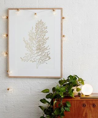 Brass battery-operated micro festoon lights from Lights4Fun hung around wall art with wooden cabinet and indoor houseplant