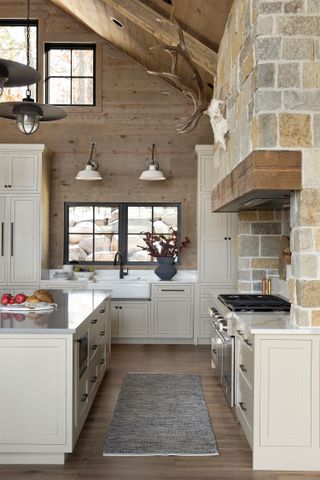 kitchen with pale painted units exposed stone above range cooker island with drawers and high windows in wooden walls