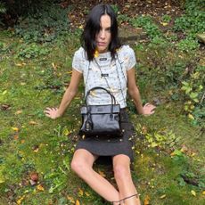 Alexa Chung sits in a garden wearing a layered top, a wool miniskirt and Miu Miu's Mary Jane loafers.