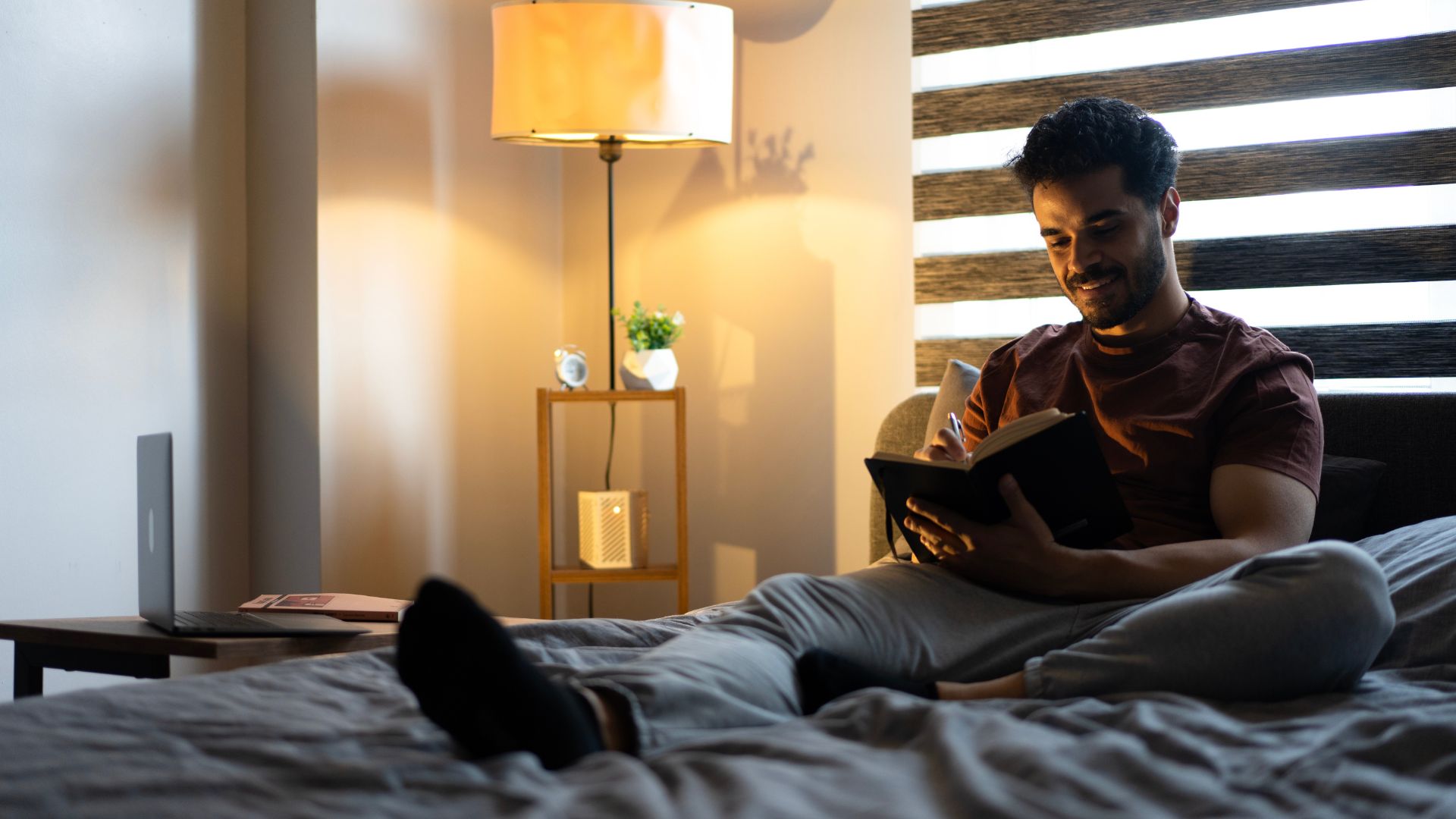 A dark-haired man writes down his worries before bed as part of the Constructive Worry Sleep Method.