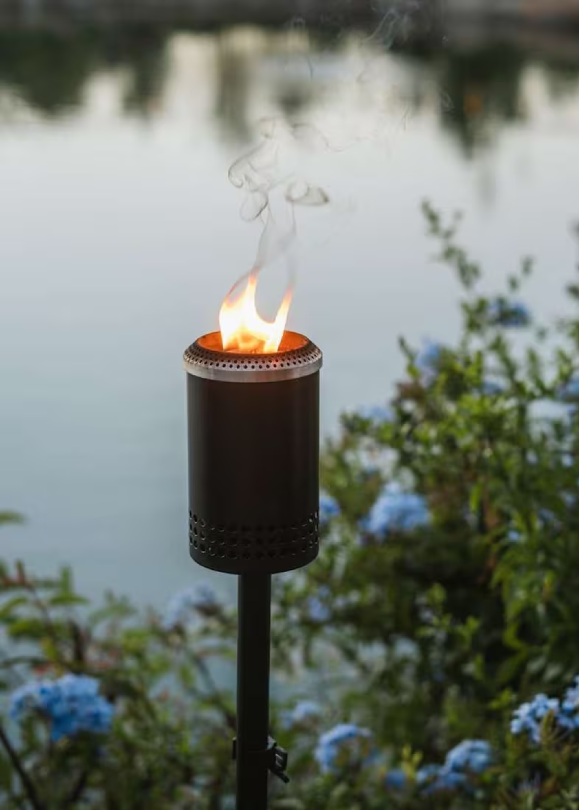 A black torch light by some blue flowers in an outdoor space