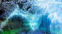 A dreamlike night landscape featuring a gravel path leading toward blooming cherry blossoms, obscured by ethereal blue and green light flares and motion blur.