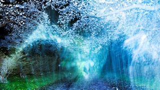 A dreamlike night landscape featuring a gravel path leading toward blooming cherry blossoms, obscured by ethereal blue and green light flares and motion blur.