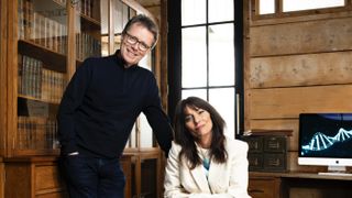 Nicky Campbell in a dark suit stands behind a seated Davina McCall in a white jacket in Long Lost Family: Born Without Trace